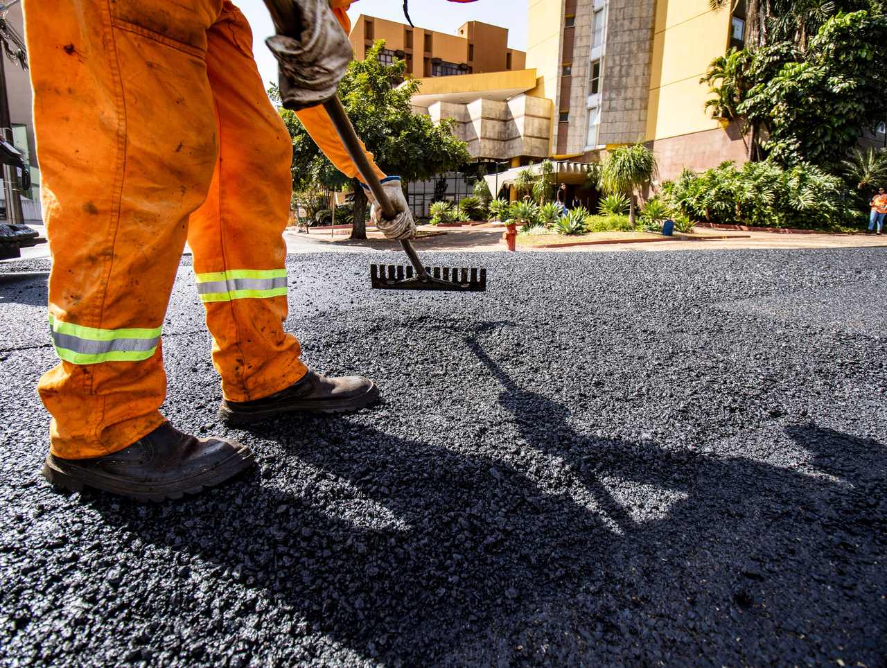 Trabajador esparciendo asfalto caliente nuevo en un estacionamiento comercial
