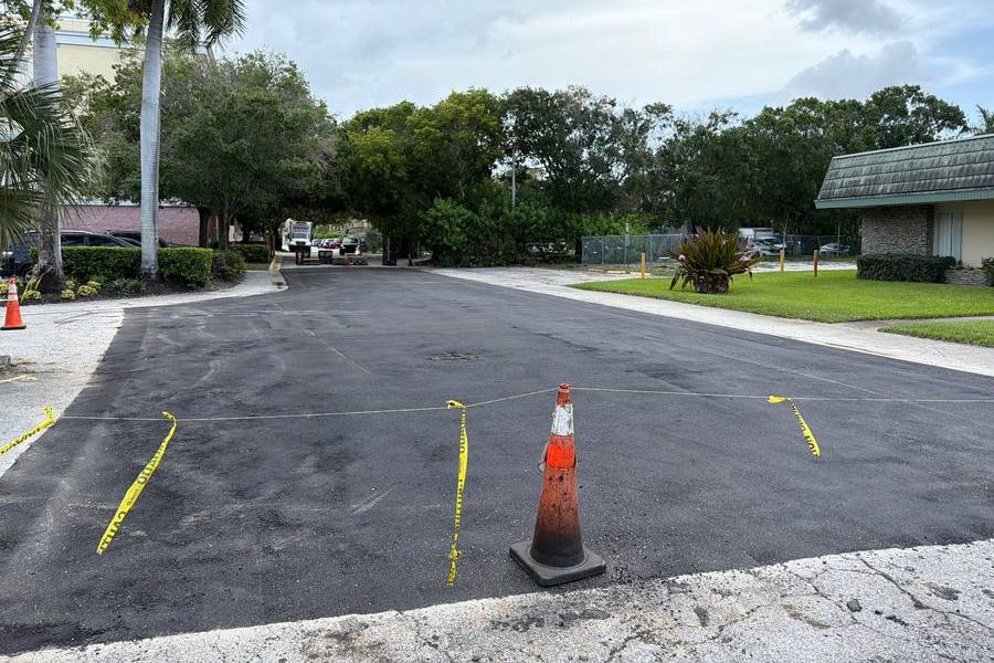 Entrada comercial recién pavimentada con asfalto, acordonada con cinta y conos después del trabajo
