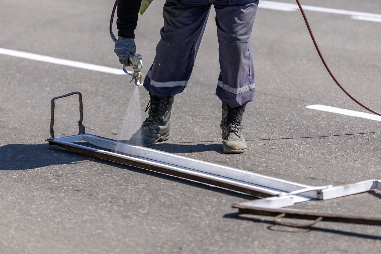 Trabajador pintando una línea blanca nueva con pistola y regla guía